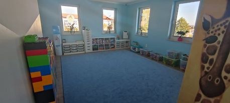 Sala z niebieskim dywanem, regałami na zabawki i malowidłem z żyrafą na ścianie