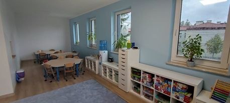 Sala ze stolikami i krzesełkami, roślinami w oknach i regałami z grami