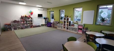 Sala z zieloną ścianą, dywanem, stolikami i regałami pełnymi zabawek