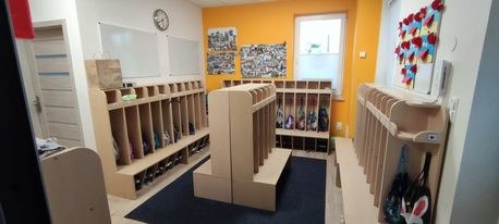 Szatnia z drewnianymi półkami na buty i wieszakami, pomarańczowa ściana